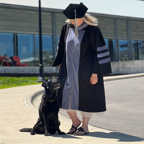 Woman wearing graduation robes, looking at dog