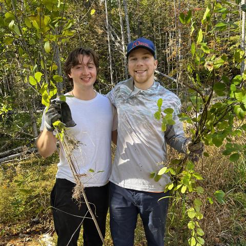 Two student volunteers holding up invasive species in the woods