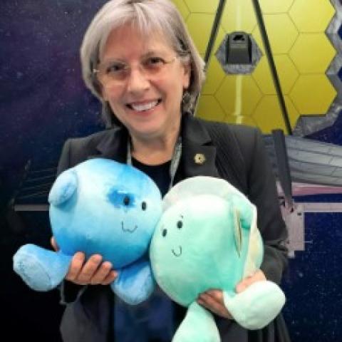 Women holding two plush toys representing planets