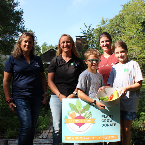 Three adults and two children in garden with Plant a Row sign