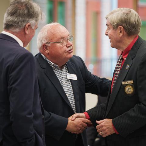 Two men shaking hands as another man looks on from the foreground.