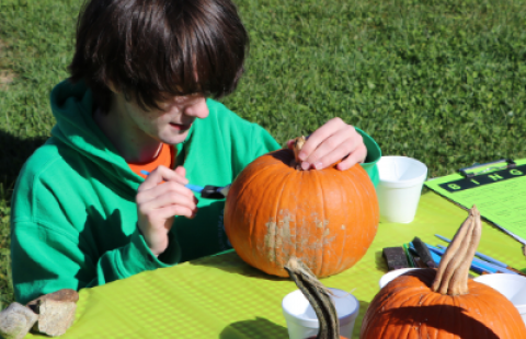 boy in green sweatshirt painting pumpkin on a table