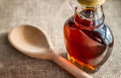 Small bottle of maple syrup on a table with a spoon