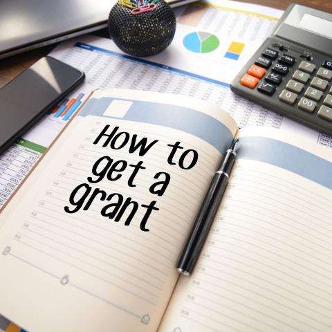 Notebook on a desk with how to get a grant written on the left side page